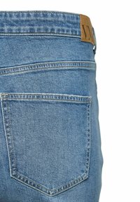 Achteraanzicht close-up van lichtblauwe spijkerbroek met een enkele gestikte achterzak en een bruin leren merklabel op de tailleband.