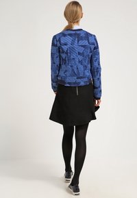 Blau gewatteierte Bomberjacke mit geometrischen Mustern, kombiniert mit einem schwarzen Rock und schwarzen Strumpfhosen, mit einer glatten Textur und figurbetontem Schnitt.