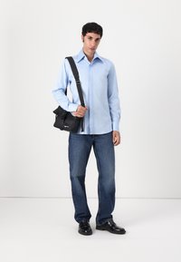 Cămașă lungă de culoare albastru deschis, blugi de culoare albastru închis și pantofi negri. Poartă o geantă neagră tip crossbody, cu clapetă și curea ajustabilă.