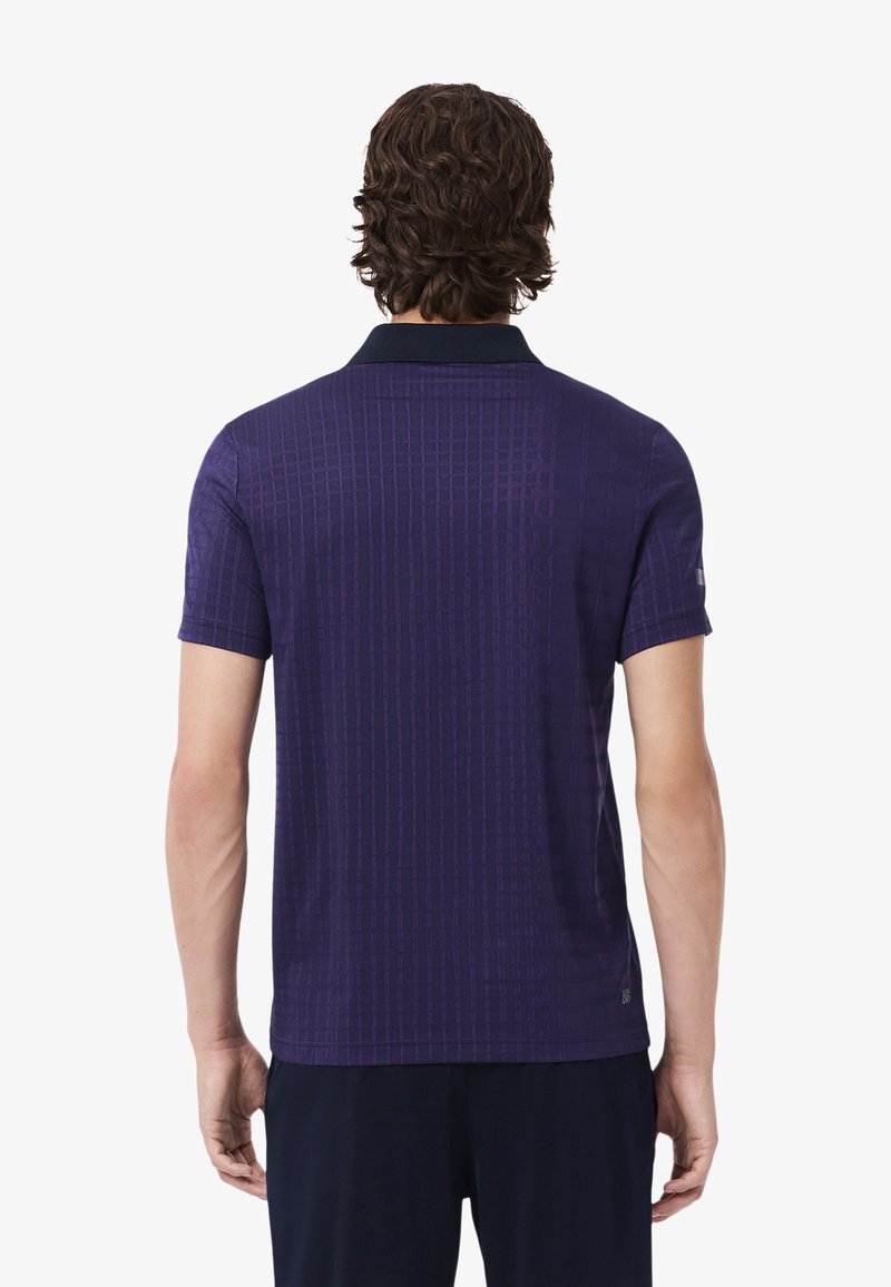 Polo a maniche corte di colore viola scuro con un motivo a griglia testurizzato e un colletto nero a contrasto. Realizzato in tessuto traspirante per il massimo comfort.