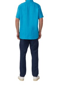 Korte mouwen, felblauw linnen shirt met een rechte zoom, gecombineerd met donkerblauwe broeken en lichtgekleurde sneakers.