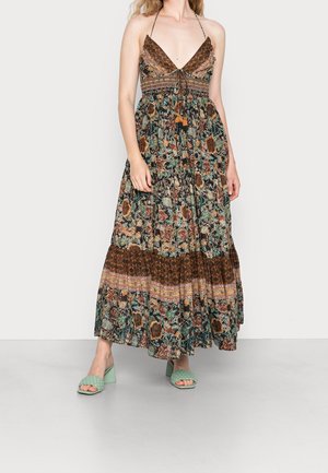 Maxi-jurk met een donker bloemenpatroon, een ruches halslijn en een geraffineerde taille. Gecombineerd met groene blokhak sandalen.