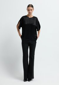Top in raso nero con maniche corte e tasche sottili, abbinato a pantaloni neri aderenti. Texture liscia e silhouette rilassata.