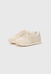 Beige New Balance sneakers with laces, suede and mesh upper, cushioned collar, and textured rubber sole on plain light background.