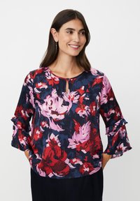Blumenbluse mit marineblauem Hintergrund und roten sowie pinken Blumen. Runder Ausschnitt mit Schlitzdetail und gerafften Ärmeln. Strukturierter Stoff.