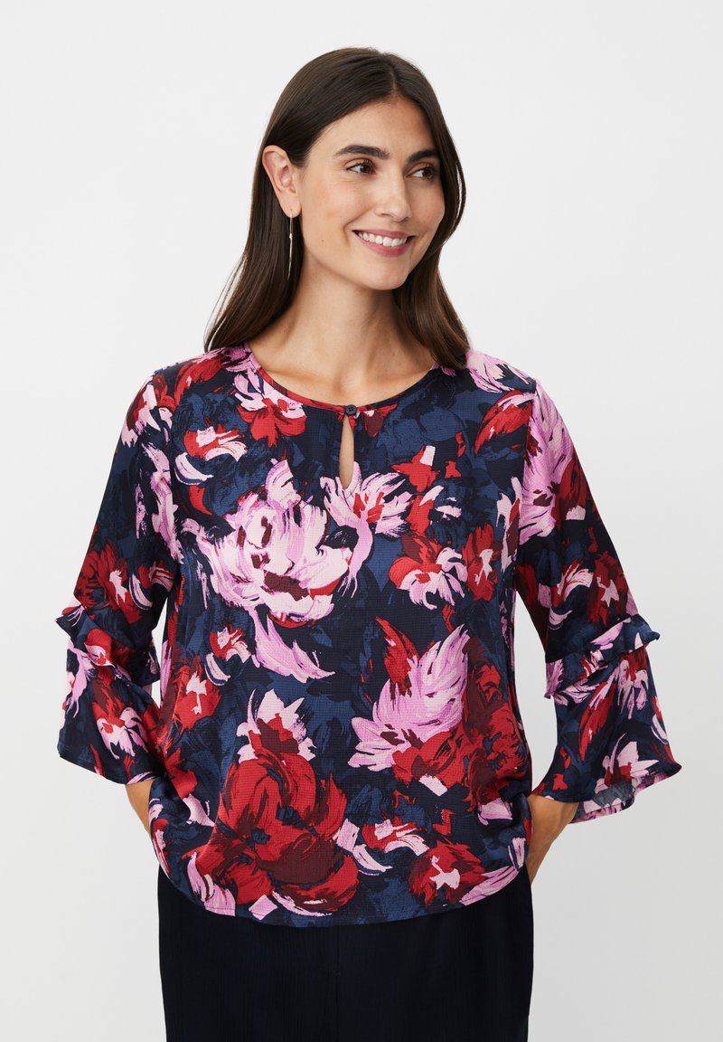 Blumenbluse mit marineblauem Hintergrund und roten sowie pinken Blumen. Runder Ausschnitt mit Schlitzdetail und gerafften Ärmeln. Strukturierter Stoff.