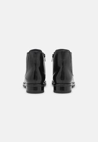 Černé kožené kotníkové boty s hladkým povrchem, vybavené zadními zipy a nízkým stohovaným podpatkem, navržené s elegantním siluetou.