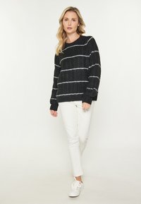 Pulover negru tricotat cu dungi orizontale albe. Are un guler rotund și mansete cu model rib. Este purtat cu pantaloni albi și adidași albi.