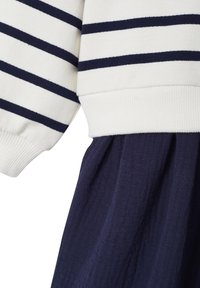 Strickkleid mit einem weißen oberen Teil und navyblauen horizontalen Streifen, mit gewirkter Textur und einem fließenden navyblauen Unterteil mit subtilen Details.