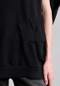 Svart oversized sweatshirt med ribbad nederkant och en sydd patchficka fram, i en slät tygkvalitet.