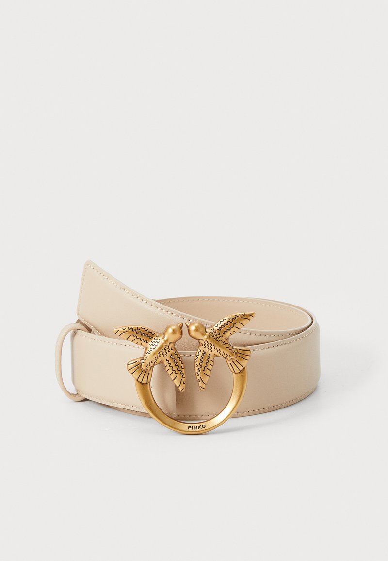 Beige leren riem met een cirkelvormige goudkleurige gesp waarop twee ingewikkeld ontworpen vogels zijn afgebeeld. Soepele textuur en strak, minimalistisch ontwerp.