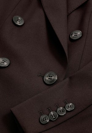 Dubbelzijdige bruine blazer met een gladde stoftextuur, voorzien van zes zwarte knopen met gegraveerde merknaam en op maat gemaakte revers.
