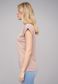 Lys rosa t-skjorte med korte rullede ermer og rund hals, kombinert med lyseblå jeans. Glatt bomullsstoff, minimal detaljer.