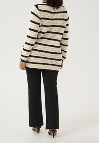 Pull en tricot crème à rayures noires, doté d'une coupe décontractée et de manches longues. Associé à un pantalon noir ajusté et des talons ouverts.