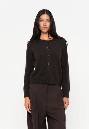 Bruine gebreide cardigan met een ronde halslijn, sluiting met knopen aan de voorkant en lange mouwen. Gladde textuur en een nauwsluitend ontwerp, gecombineerd met donkere broeken.