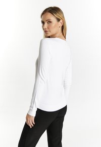 Witte langemouw fitted top met een ronde hals, gemaakt van zacht materiaal. Beschikt over ribgebreide manchetten en onderzoom, gecombineerd met zwarte broek.