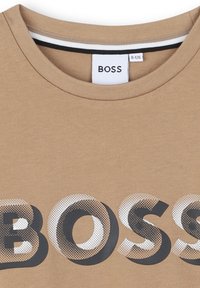 T-shirt brown a maniche corte con audace logo "BOSS" in un motivo in bianco e nero a punti, colletto rotondo e dettagli a righe sottili.
