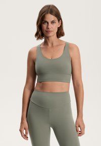 Sports bra and high-waisted leggings in muted green fabric. The bra features wide straps and a seamless design with a smooth texture.