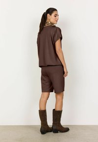 Top corto a maniche corte marrone e pantaloni corti abbinati, realizzati in tessuto morbido. Indossato con stivali marroni fino al ginocchio. Sciarpa con stampa leopardata visibile al collo.