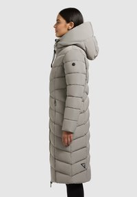 Langer, hellgrauer Puffermantel mit Kapuze, diagonal gesteppten Mustern, einem Frontreißverschluss und einem Logo-Patch am Saum.