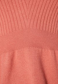 Pull en corail à côtes avec un motif en V dans la partie supérieure, doté de rayures verticales texturées et d'une finition douce en tricot.
