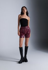 Black strapless top, deep burgundy leather shorts with a belt, and knee-high black platform boots. Smooth textures and structured silhouette.