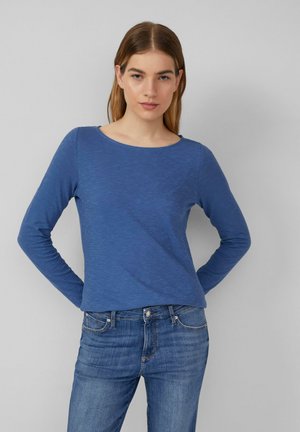 T-shirt bleu à manches longues avec un col ras du cou, en tissu texturé et à coupe décontractée, associé à un jean bleu délavé.