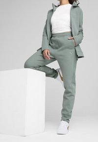 Lichtgroene trainingspak met een jack met rits en broek met elastische tailleband. Gecombineerd met witte sneakers met gouden accenten. Glad oppervlak.