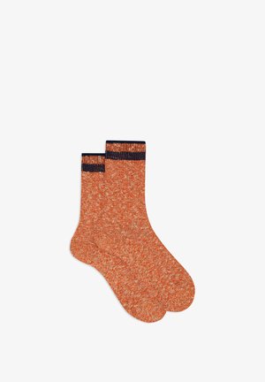 Calze arancioni lavorate a maglia con un motivo testurizzato, caratterizzate da un bordo a costine di colore blu marino. Le calze hanno un'altezza fino al polpaccio e sono esposte in posizione verticale.