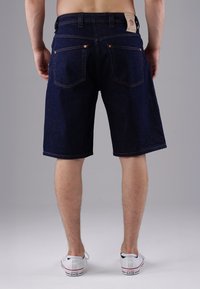 Dark blue denim shorts with a straight cut, featuring two back pockets and copper rivets. Worn with white sneakers.