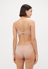 Lys beige undertøysett med en glatt, sømløs BH med justerbare stropper og en matchende truse med bølget blondekant.