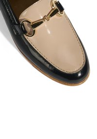 Zwarte en beige leren instappers met een glanzende afwerking, voorzien van een goudkleurige kettingaccent aan de voorkant en een ronde neusvorm.