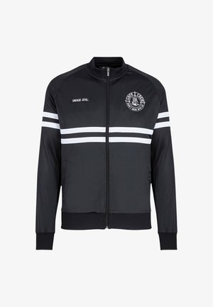 Chaqueta atlética negra con rayas blancas, cierre de cremallera y un logo redondo. Fabricada con tela suave, cuenta con puños y dobladillo acanalados.