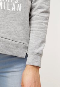 Sudadera gris con texto blanco, con puños y dobladillo acanalados, textura suave, corte relajado y escote en crew.