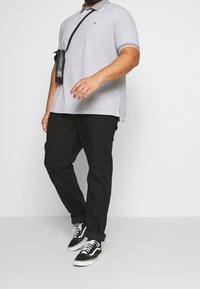 Světle šedé polokošile s límečkem, kontrastním lemováním, spárovaná s černými kalhotami a černými teniskami. Obsahuje malou černou crossbody tašku.