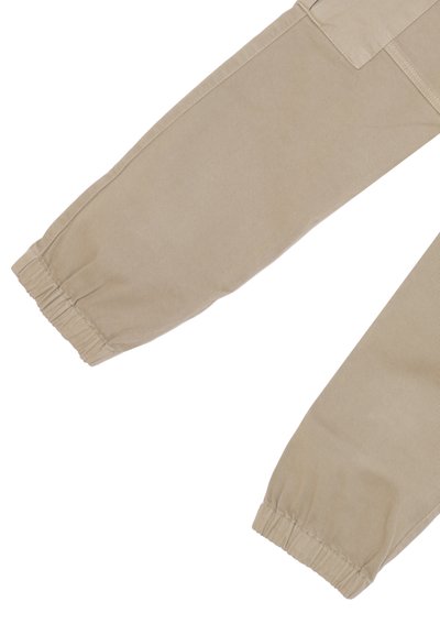 Pantaloni beige in cotone con polsini elasticizzati, visti dalla ginocchia in giù, contro uno sfondo bianco.