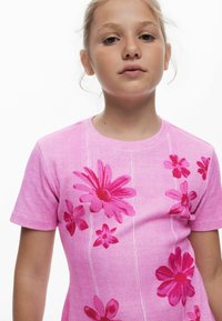 Rosa gestricktes T-Shirt mit kurzen Ärmeln, das große Blumenmuster in verschiedenen Pinktönen zeigt, mit rundem Ausschnitt und dezenten vertikalen Linien.