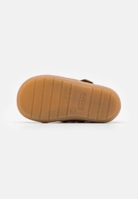 Brown sandal with a textured rubber sole, adjustable strap, and a cushioned footbed. The sole features patterned grip lines for traction.