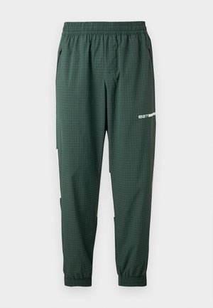 Donkergroene taps toelopende trainingsbroek met elastische tailleband en boorden, subtiel ruitpatroon, ritssluitingen aan de zijkanten en een wit "ea7" logo op het bovenbeen.