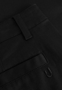 Černá látka s plochým pasem a prošitými detaily. Obsahuje zadní kapsu s jemně embosovaným logem. Hladká textura, bez vzorů.