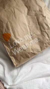Sac en papier kraft avec texture froissée ; présente un graphique orange et un texte blanc disant "Aime-moi. Porte-moi." sur le devant.