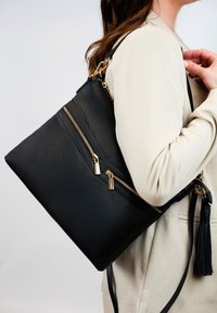 Zwarte leren tote bag met meerdere ritsen, gouden hardware-accenten en een gestructureerde afwerking. Inclusief een kwastje en een verstelbare schouderband.