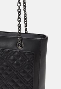 Czarna skórzana torebka z pikowanym panelem z przodu i srebrnymi łańcuszkowymi ramiączkami na tle białym.