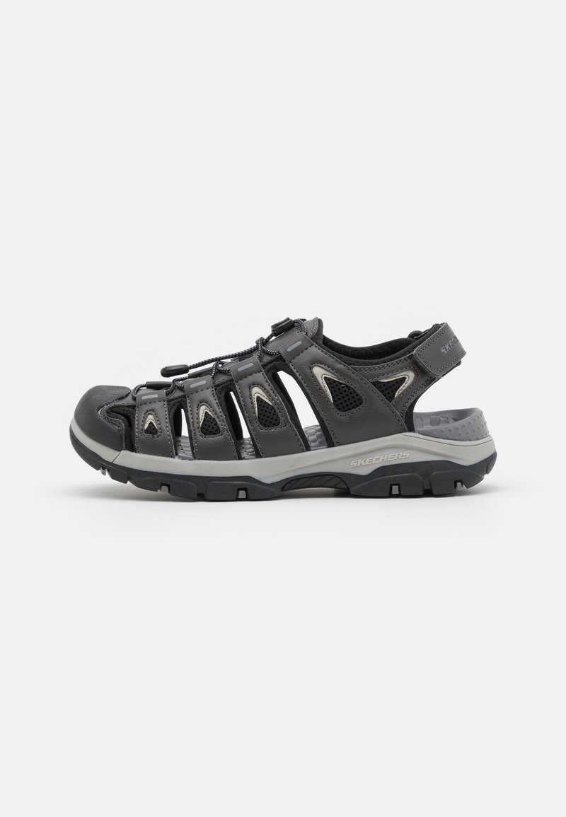 Black sandal featuring a mesh upper, adjustable strap, protective toe cap, and rubber sole with traction grooves. Accented with gray details.