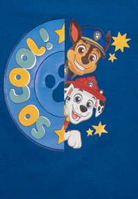 Maglietta in cotone blu con una grafica circolare che presenta cani dei cartoni animati, il testo "SO COOL!" e accenti di stelle gialle. Design stampato, vista frontale.