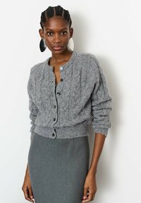 Hallimehe hall kudumiga kardigan, millel on kaablipattern, ümar kaelus ja nööpidega kinnitused. Varustatud soonikohtade ja hemiga, et luua vormitud siluett.