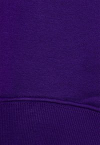 Tela de sudadera morada con textura suave, puños acanalados y costuras planas. Presenta un color uniforme sin patrones ni acentos.