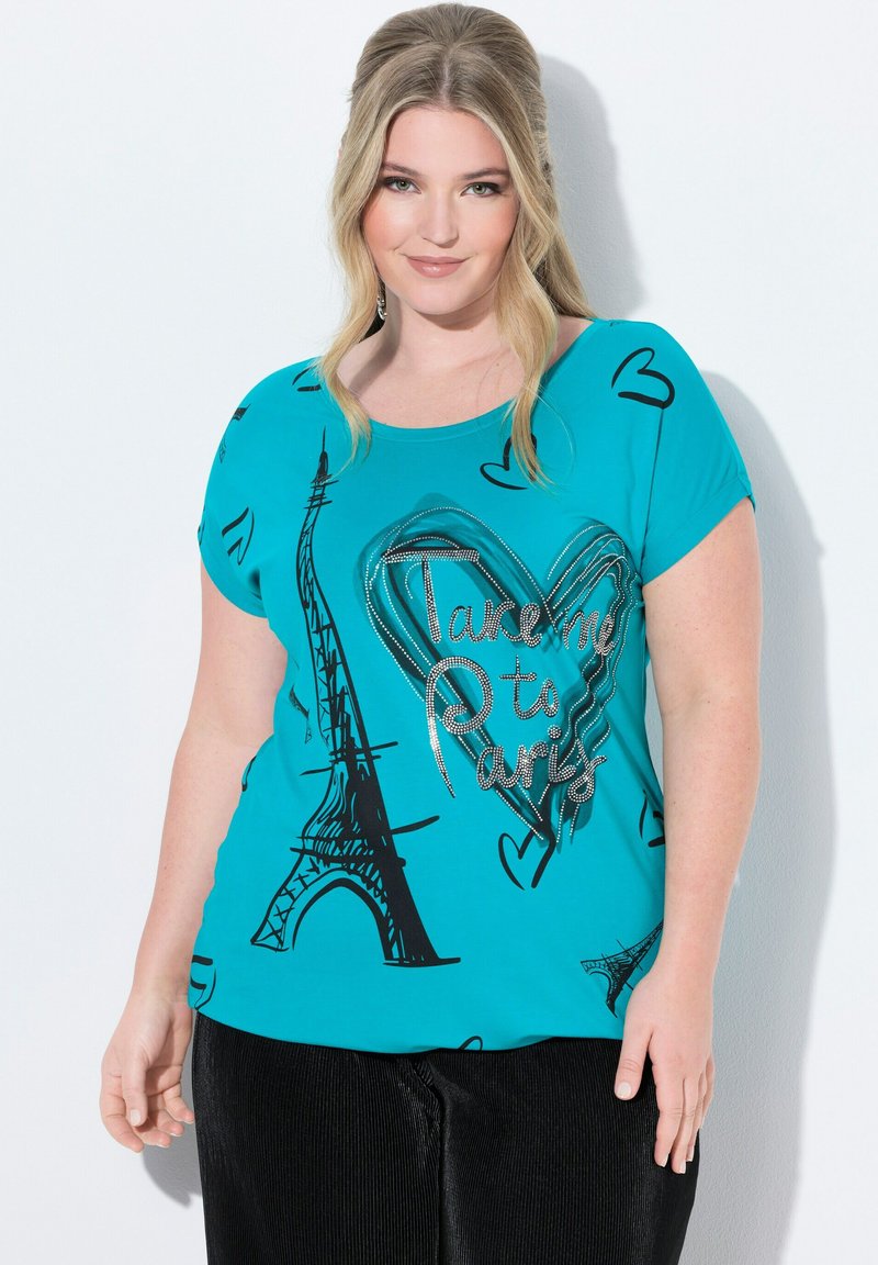 T-paita turkoosilla taustalla, jossa on musta Eiffel-torni ja sydängrafiikka, ja teksti "Vie minut Pariisiin" kiiltävällä hopeakirjailulla. Lyhyet hihat.