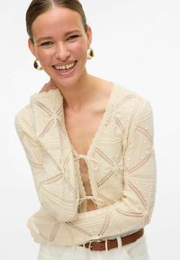 Romige gebreide top met een diepe V-hals, met ingewikkelde patronen, geschulpte randen en een striksluiting.