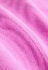 Detailný záber mäkkej ružovej rebrovanej látky ukazujúci jej textúru a jemné záhyby.